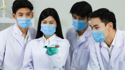 Group of doctors and researchers standing together and looking to test tube on hand of female