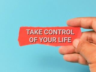 Phrase TAKE CONTROL OF YOUR LIFE on red strip paper hand held isolated on blue background.