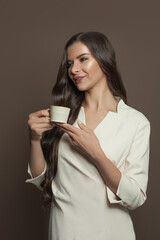 Beautiful brunette woman drinking coffee on brown background