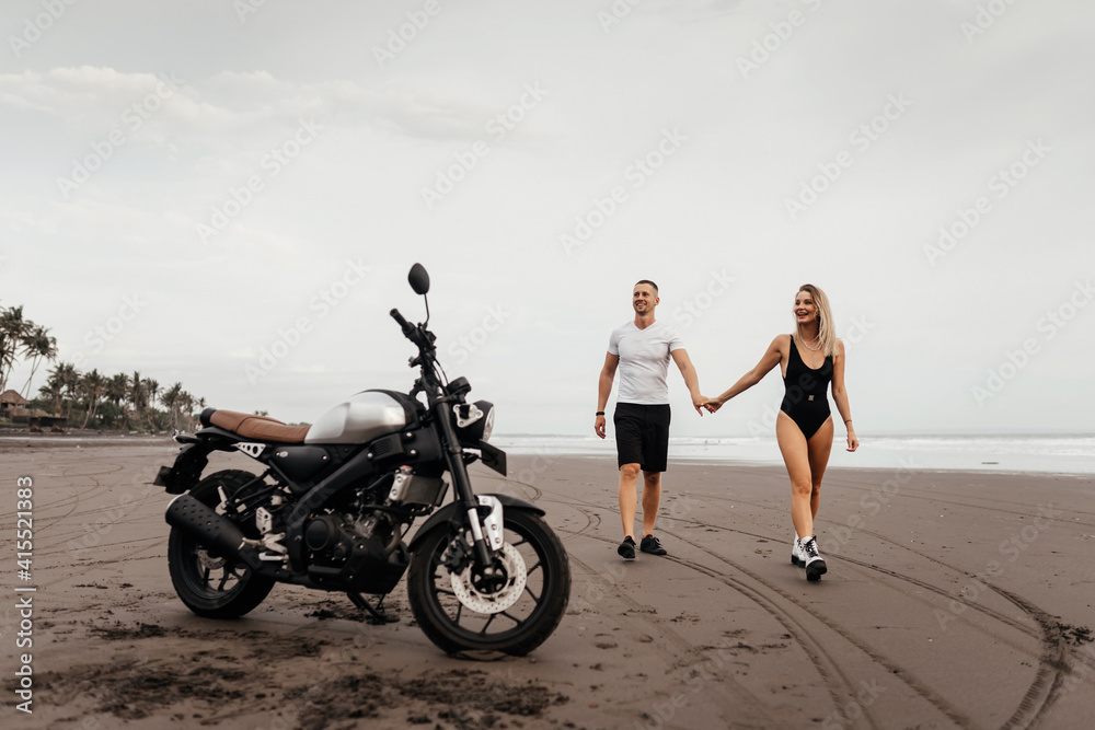 Wall mural Young couple riders together on sand beach by motorbike - travel concept