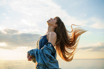 beautiful young woman with fluttering long hair against the sky in a denim jacket