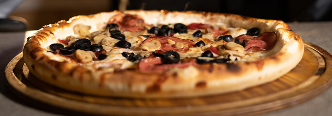 American pizza with olives on a round board on a table in a pizzeria. Banner for pizzeria and bakery.