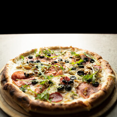 Pizza with cheese, salami and olives on a round wooden board on a gray background close-up. Ready-made pastries.