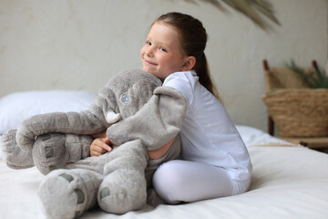 Sweet little girl sitting on her bed at home with toy elephant.
