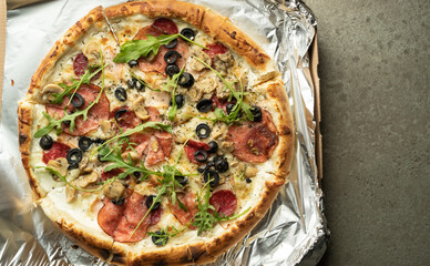 On the table there is hot pizza with olives, salami and mozzarella on foil. Copy space. Italian pastries.