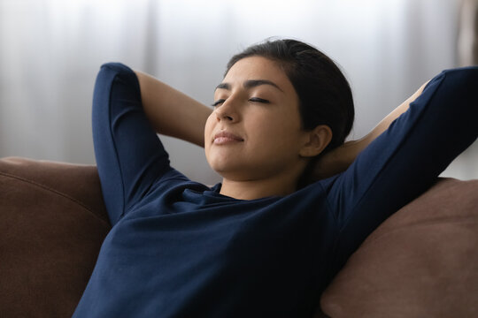 Happy calm millennial Indian woman lying relaxing on sofa in living room sleep or take nap. Relaxed young mixed race female rest on couch at home daydream relive negative emotions. Peace concept.