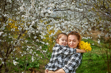 Fototapeta premium Mother and daughter on the background of flowering trees on a spring walk