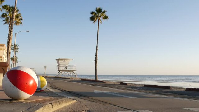 Pacific ocean beach, Oceanside California USA. Ball, lifeguard tower, life guard watchtower hut and tropical palm tree, sky, beachfront street, waterfront road. Los Angeles vibes, aesthetic atmosphere