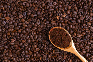 Ground coffee in a wooden spoon lies on freshly roasted coffee beans