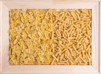 Farfalle and fusilli pasta in a wooden frame. Top view
