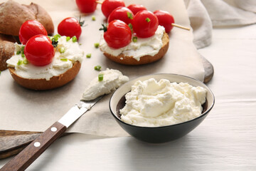 Bowl with tasty cream cheese on light wooden background