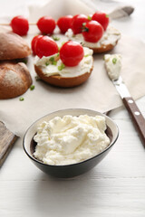 Bowl with tasty cream cheese on light wooden background