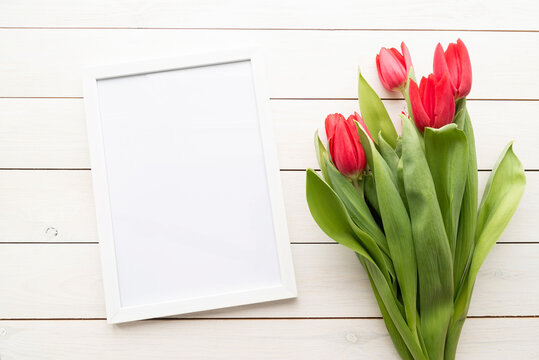 White frame with spring tulips top view over white wooden background