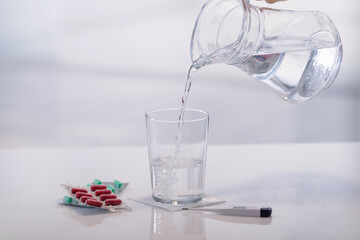 Hand pouring water into a glass next to medication