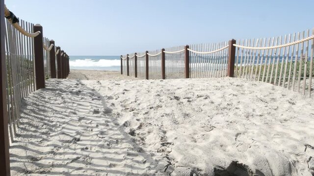 Pacific ocean coast, greenery and wooden picket fence on sea shore. Blue water waves on sunny summer beach, Encinitas shoreline, California USA. Coastline near Los Angeles. Coastal access entrance.