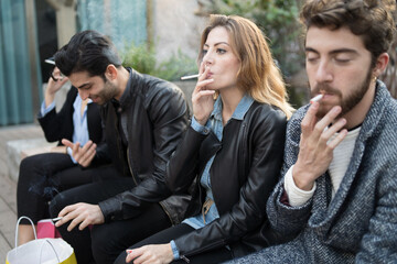 Bad habits - group of young friends smoking cigarettes together outdoors. Unhealthy addiction concept. © Lomb