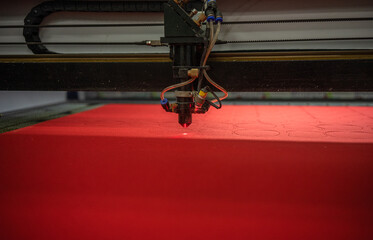 laser machine cuts out details on red fabric