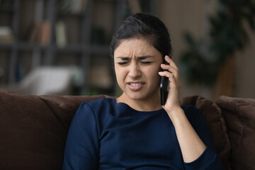 Upset young Indian woman talk on smartphone at home feel distressed disappointed with bad news....