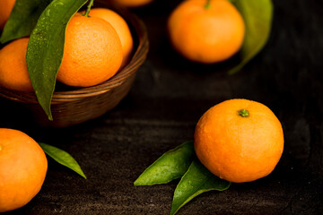 Dark mood fresh orange clementines with green leaves in a basket on a dark table