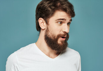 Obraz premium Portrait of an emotional man in a white t-shirt on a blue background and a thick beard mustache model
