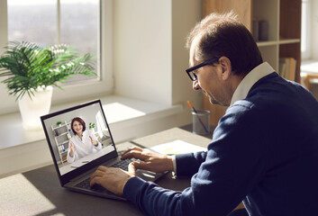 Obraz na płótnie Canvas Male patient consulting online doctor at home. Mature man using laptop computer and communicating with nurse or general practitioner. Telemedicine, virtual visit to clinic, video conference concept