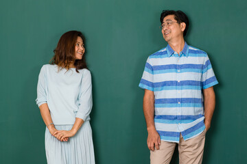 middle-aged Asian man and woman, couple dress casually smiling and standing against green background. Studio shot for concept of happiness and warmth family