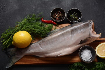 Fresh raw salmon red fish with spices, lemon, pepper, on dark stone background.