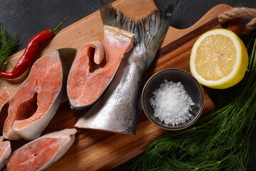 Fresh raw salmon steaks on board with salt, peppers, lemon,  on black background,