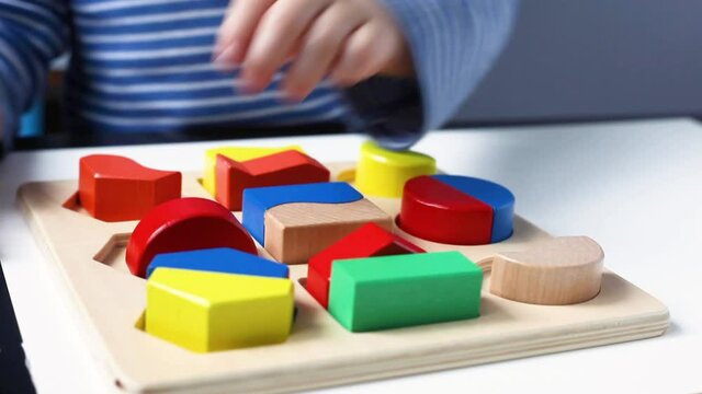 Educational toys, Cognitive skills, Montessori activity. Closeup: Hands of a little Montessori kid learning about color, shape, sorting, arranging by engaged colorful wooden sensorial blocks. 