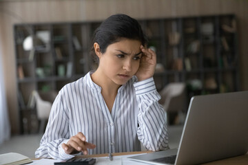 Unhappy millennial Indian woman pay bills online on computer have problems with budget planning....