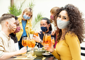 Young friends drinking cocktails wearing protective face mask - New normal lifestyle concept with people enjoying happy hour at cocktail bar - Food, drink and people concept.