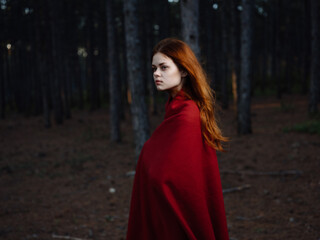 A red-haired woman with a plaid on her shoulders walks in the forest near the trees