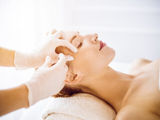 Beautiful woman receiving beauty injections with closed eyes in sunny medical center. Beautician doctor hands doing beauty procedure to female face with syringe. Cosmetic medicine and surgery concept