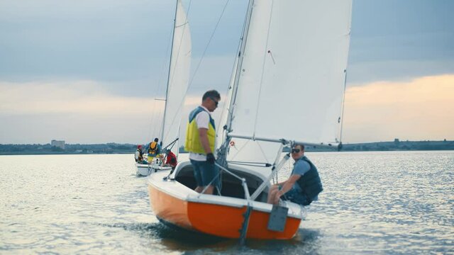 Adult professional sailors in life vests driving luxury yachts on beautiful carm river. Sailboats. Sailing yacht. Water activity in summer. Freedom concept.