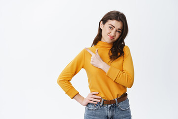 Skeptical girl express dislike and doubts, grimacing over bad promotion, pointing finger left at...