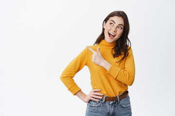 Cheerful pretty female model say yes, pointing and looking left at empty space, making decision,...