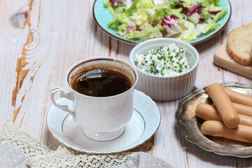 Breakfast table with cup of coffee, healthy salad, cottage and sausages.