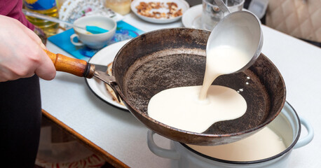 The dough for pancakes is poured into a frying pan. Preparation for the celebration of Maslenitsa. Selective focus.