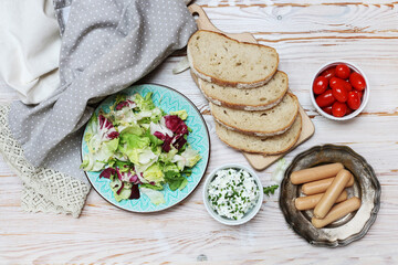 Breakfast table with fresh salad, cottage, sliced bread and sausages.