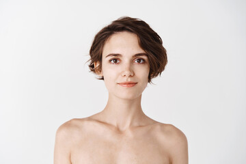 Skincare. Young caucasian woman with short hair and naked body, smiling at camera. Girl with hydrated skin looking happy after applying daily care facial cream, white background