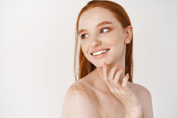 Skincare and beauty. Close-up of young woman with pale skin and freckles standing naked on white...