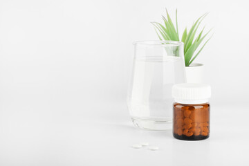 pills in glass bottle, green plant in pot and glass of water on white background. medicine and healthcare concept. copy space
