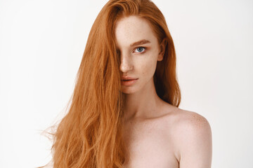 Close-up of beautiful young woman with long healthy red hair looking at camera. Pale female redhead model gazing sensual, white background