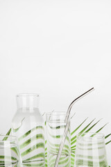 palm leaf distorted through water in glasses and bottle with reusable tube on white background. Home decor, eco friendly,pure water concept.copy space