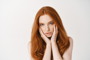 Beauty. Close-up of natural young woman with ginger hair, touching pale clean no make-up face and...