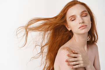 Close-up of tender young woman with long natural red hair flying in air, close eyes and relaxing on...