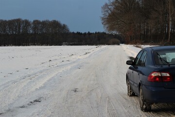 Blue car on snowy dirt road next to a field