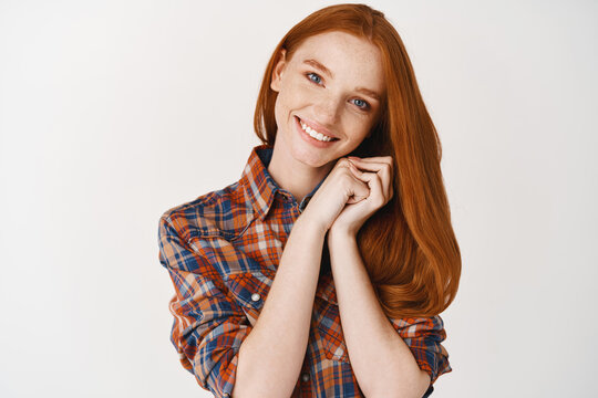 Beauty. Image of beautiful redhead teenage girl admiring something, looking dreamy at camera, smiling with white teeth, standing over white background