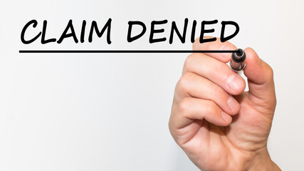 the hand writes text CLAIM DENIED with a marker on a white background. business concept