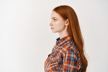 Profile of young woman with long healthy ginger hair and pale skin, looking left with serious face,...